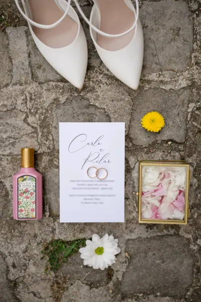 Partecipazione, fedi, scarpe e petali della sposa sul selciato in pietra